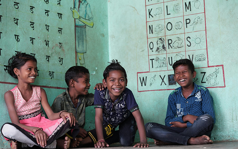 Four smiling children sitting on the floor in a classroom