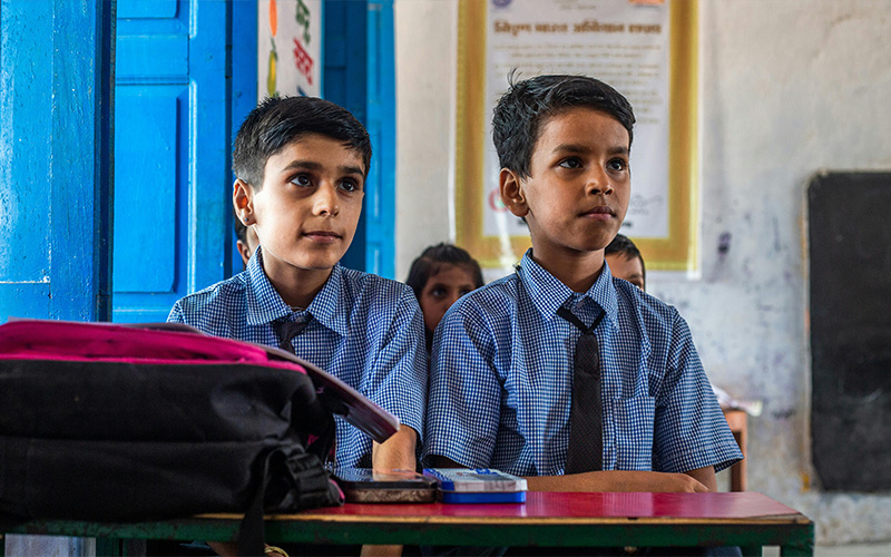 Two young boys in school uniforms sitting at a desk in a classroom
