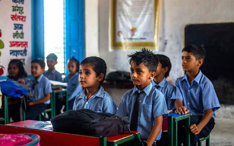 A group of young school children in blue checkered shirts sitting at desks in a classroom